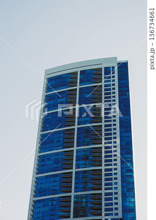 Tall building with blue glass windows standing against a clear sky during the day in an urban area Tall building with blue glass windows standing against a clear sky during the day in an urban area 136734661