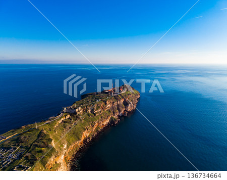 View of coastal land and ocean from above showing a cliff and water on a clear day with blue sky and few clouds View of coastal land and ocean from above showing a cliff and water on a clear day with blue sky and few clouds 136734664