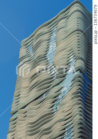 Wavy building structure located in an urban area with a clear blue sky showcasing modern architecture during daylight hours Wavy building structure located in an urban area with a clear blue sky showcasing modern architecture during daylight hours 136734679