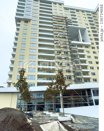 Construction of a tall building with scaffolding and landscaping work during daylight in an urban area 136734688