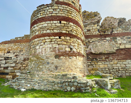 Ruins of an old stone tower stand in a grassy area with remnants of walls and historical structures during a sunny day Ruins of an old stone tower stand in a grassy area with remnants of walls and historical structures during a sunny day 136734713