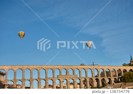 A Hot air balloon offers breathtaking views above the magnificent Aqueduct of Segovia, with swallows soaring gracefully nearby. 136734776