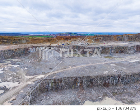 Open land used for mining with machinery working in a large quarry under cloudy skies in an industrial setting Open land used for mining with machinery working in a large quarry under cloudy skies in an industrial setting 136734879