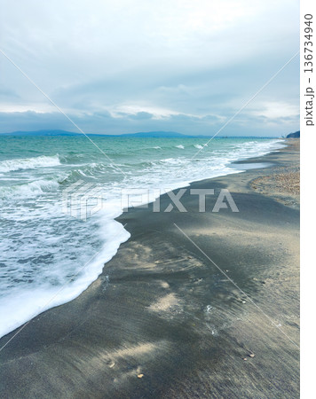 Waves rolling onto a beach with clouds in the sky over the water during the day by a coastal area in a serene location Waves rolling onto a beach with clouds in the sky over the water during the day by a coastal area in a serene location 136734940