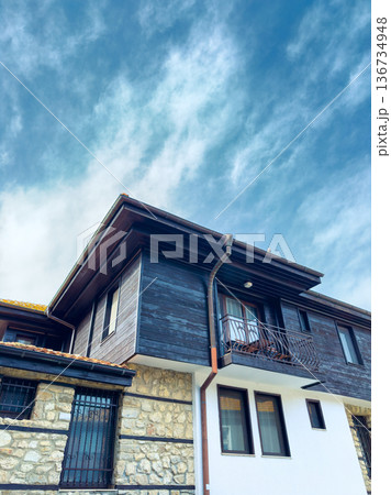 Wooden and stone building with balcony under a blue sky and clouds during daytime in a rural setting Wooden and stone building with balcony under a blue sky and clouds during daytime in a rural setting 136734948