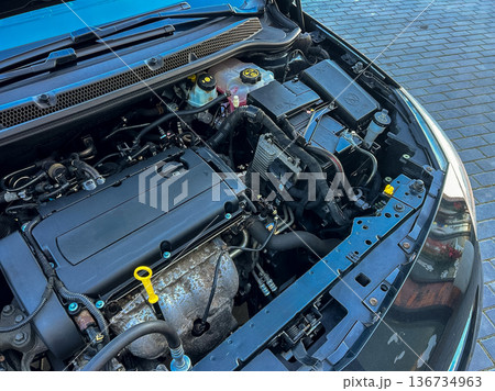Close look at car engine showing various parts and components while parked in garage during daytime on paved surface Close look at car engine showing various parts and components while parked in garage during daytime on paved surface 136734963