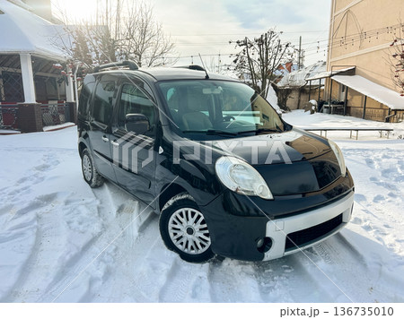 Black van parked in snowy area with trees and buildings nearby during daylight hours 136735010