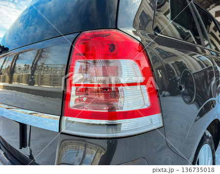 Close view of a car tail light showcasing design and details under clear skies with reflections visible on the vehicle surface Close view of a car tail light showcasing design and details under clear skies with reflections visible on the vehicle surface 136735018