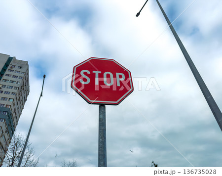 Stop sign stands tall beside tall buildings and street lamps under a cloudy sky in an urban area during the day Stop sign stands tall beside tall buildings and street lamps under a cloudy sky in an urban area during the day 136735028
