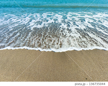 Waves rolling onto sandy beach with clear blue water on sunny day at the coast 136735044