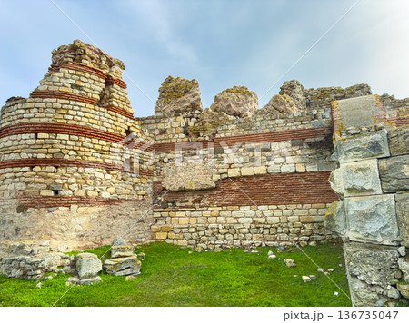 Ruins of an ancient stone structure with grass and blue sky visible in the background during daytime hours Ruins of an ancient stone structure with grass and blue sky visible in the background during daytime hours 136735047