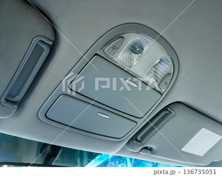 Interior view of a car's overhead control panel with lights and switches located above the driver's seat for adjusting settings and lighting 136735051