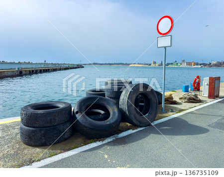 Old tires are stacked near the harbor by the water under a cloudy sky with a no entry sign beside them Old tires are stacked near the harbor by the water under a cloudy sky with a no entry sign beside them 136735109