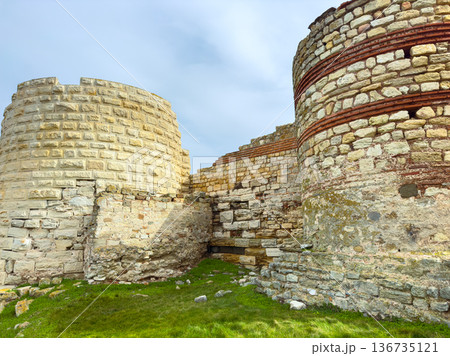 Ruins of an ancient stone structure located in a historical site with visible layers and features under a cloudy sky 136735121