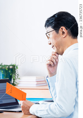 年金手帳を見ながら考える中高年男性 年金手帳を見ながら考える中高年男性 136735723