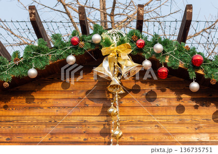 Festive christmas garland with gold bells on wooden cabin roof at outdoors Christmas market Festive christmas garland with gold bells on wooden cabin roof at outdoors Christmas market 136735751