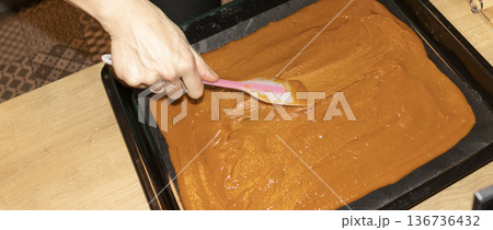 Person spreads, brown, heavy, sugary cream on a baking tray Person spreads, brown, heavy, sugary cream on a baking tray 136736432