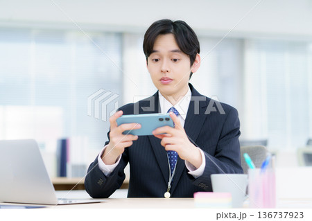 オフィスでスマホで動画視聴する若い日本人男性 オフィスでスマホで動画視聴する若い日本人男性 136737923