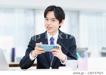 オフィスでスマホで動画視聴する笑顔の若い日本人男性 オフィスでスマホで動画視聴する笑顔の若い日本人男性 136737925