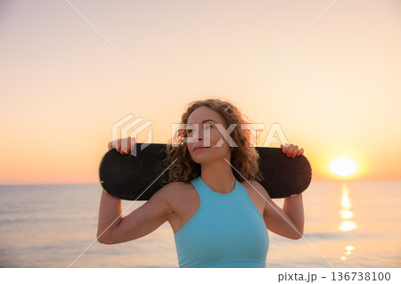 Fit young woman posing against sea background. Sporty female with skateboard on the seaside promenade. 136738100