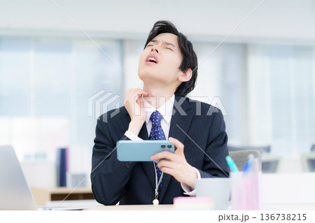 オフィスでスマホで動画視聴しながら首をかく若い日本人男性 136738215