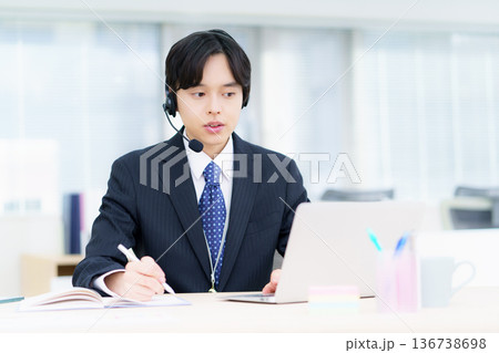 オフィスでヘッドセットをつけてパソコンに向かって会話する若い日本人男性 136738698