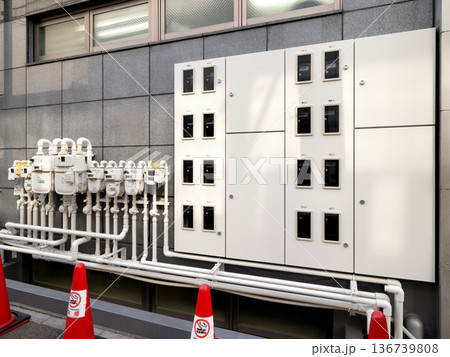 ビルの外壁に並ぶ複数のガスメーターと配電盤 136739808