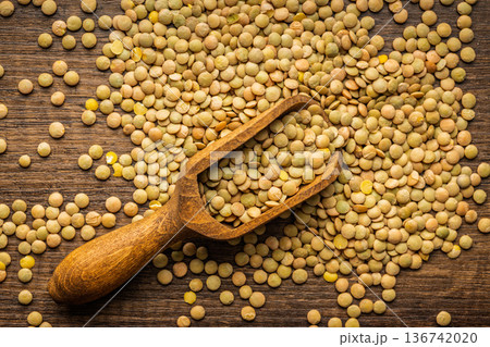 Uncooked green lentil on scoop on wooden table. Top view. 136742020