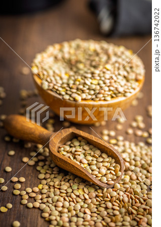 Uncooked green lentil on scoop on wooden table. Uncooked green lentil on scoop on wooden table. 136742022