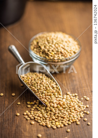 Uncooked green lentil on scoop on wooden table. Uncooked green lentil on scoop on wooden table. 136742024
