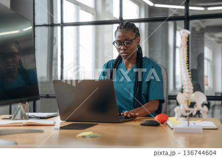Table with laptop, woman is sitting. Female doctor in coat is in the office clinic Table with laptop, woman is sitting. Female doctor in coat is in the office clinic 136744604