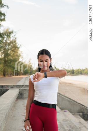 Fit Asian Woman in Sportswear Standing Outdoors in Park Environment Using Smartwatch Fit Asian Woman in Sportswear Standing Outdoors in Park Environment Using Smartwatch 136744767