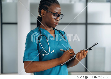 Writing information into documents. Female doctor is indoors in modern room Writing information into documents. Female doctor is indoors in modern room 136745267