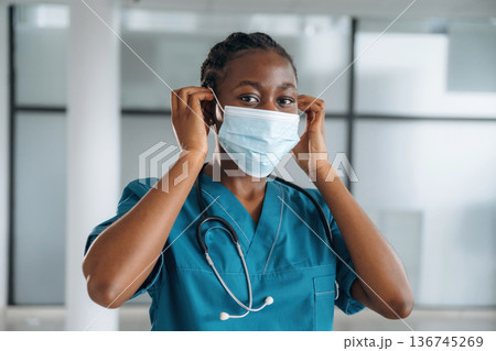 Wearing the mask. Female doctor is indoors in modern room Wearing the mask. Female doctor is indoors in modern room 136745269