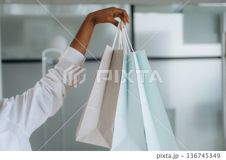 Close up view of woman's hand that is holding shopping bags indoors 136745349
