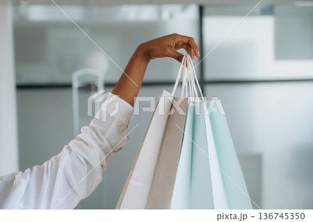 Close up view of woman's hand that is holding shopping bags indoors Close up view of woman's hand that is holding shopping bags indoors 136745350