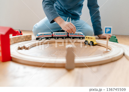 Toddler playing with wooden train railway on floor at home. Cozy indoor family activity in modern apartment, natural light, early childhood bonding and mindful parenting concept 136745509