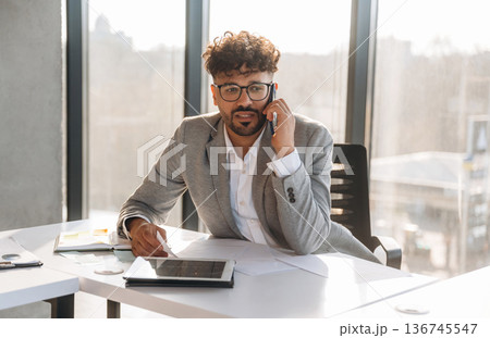 Making a call, talking by phone. Businessman is sitting in the office 136745547