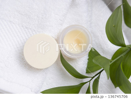 Opened balm jar with natural herbal salve on white towel near green leaves, skincare product Opened balm jar with natural herbal salve on white towel near green leaves, skincare product 136745706