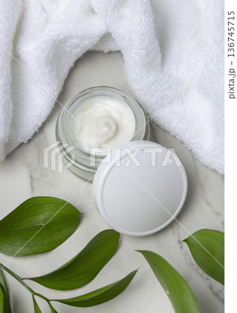 Cosmetic mockup, opened face cream jar with blank lid near white bath towel and green leaves 136745715