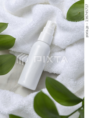 Mockup of blank white spray bottle on white bath terry towel with green leaves. Unbranded cosmetic 136745717