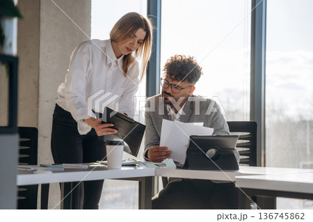 Against window, with documents. Man and woman are indoors in modern building Against window, with documents. Man and woman are indoors in modern building 136745862