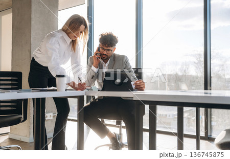 Working on a project together. Man and woman are indoors in modern building Working on a project together. Man and woman are indoors in modern building 136745875
