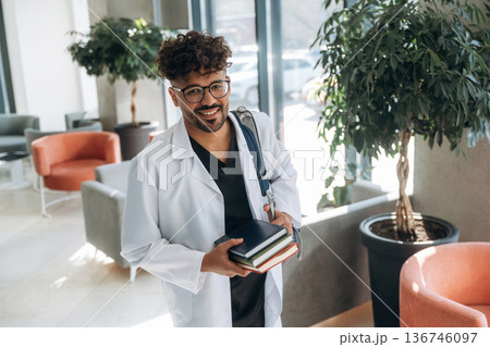 Bunch of books in hands. Man is indoors in the modern building 136746097