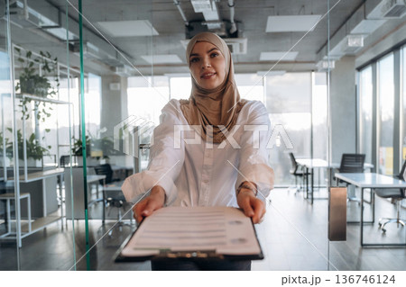 Paperwork, documents in hand. Muslim woman in hijab is in the office Paperwork, documents in hand. Muslim woman in hijab is in the office 136746124
