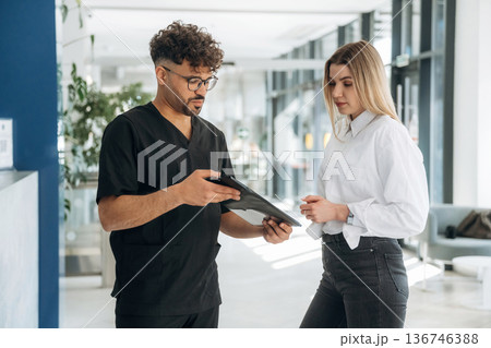Showing information in notepad. Man and woman are indoors in modern building Showing information in notepad. Man and woman are indoors in modern building 136746388