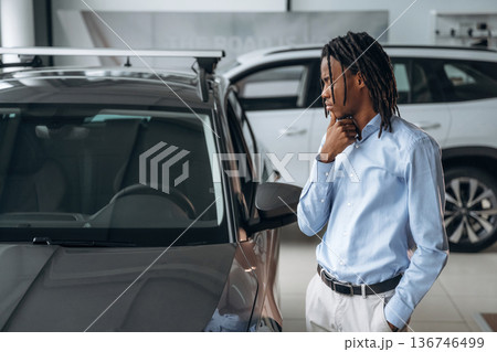 View from the side, looking at vehicle. Car seller, businessman is standing in automobile salon 136746499