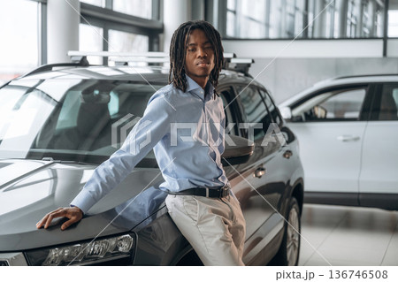 Leaning on the vehicle. Car seller, businessman is standing in automobile salon 136746508