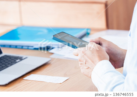 パソコンとスマホで確定申告の準備をする男性 136746555