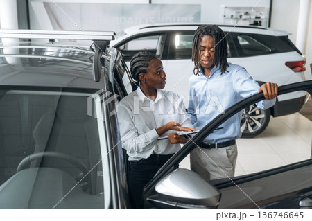 Doors are opened, looking inside. Car seller is assisting client in the automobile salon 136746645